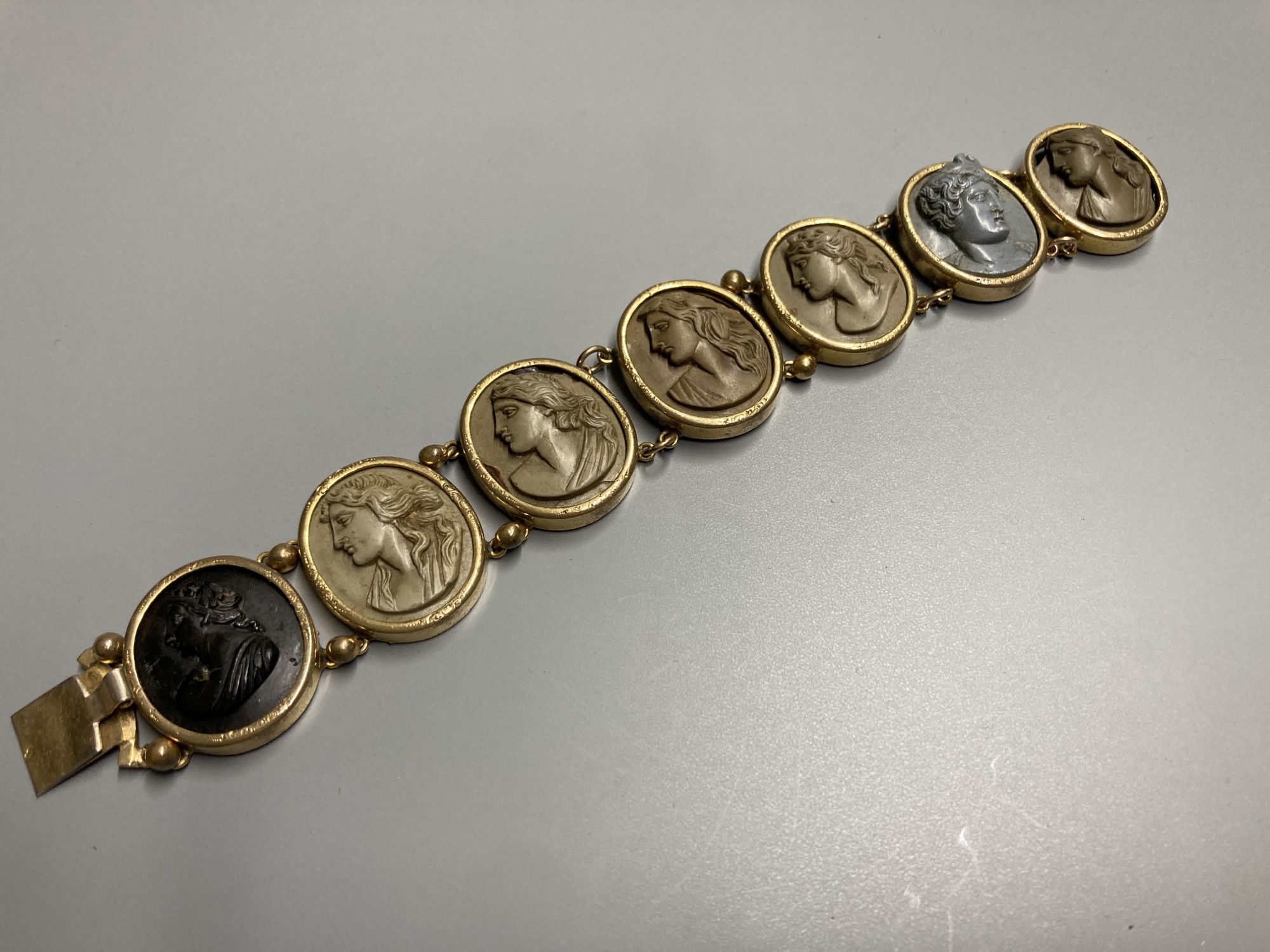 A late Victorian gilt metal bracelet set with seven oval lava plaques carved with busts of ladies, 17cm.